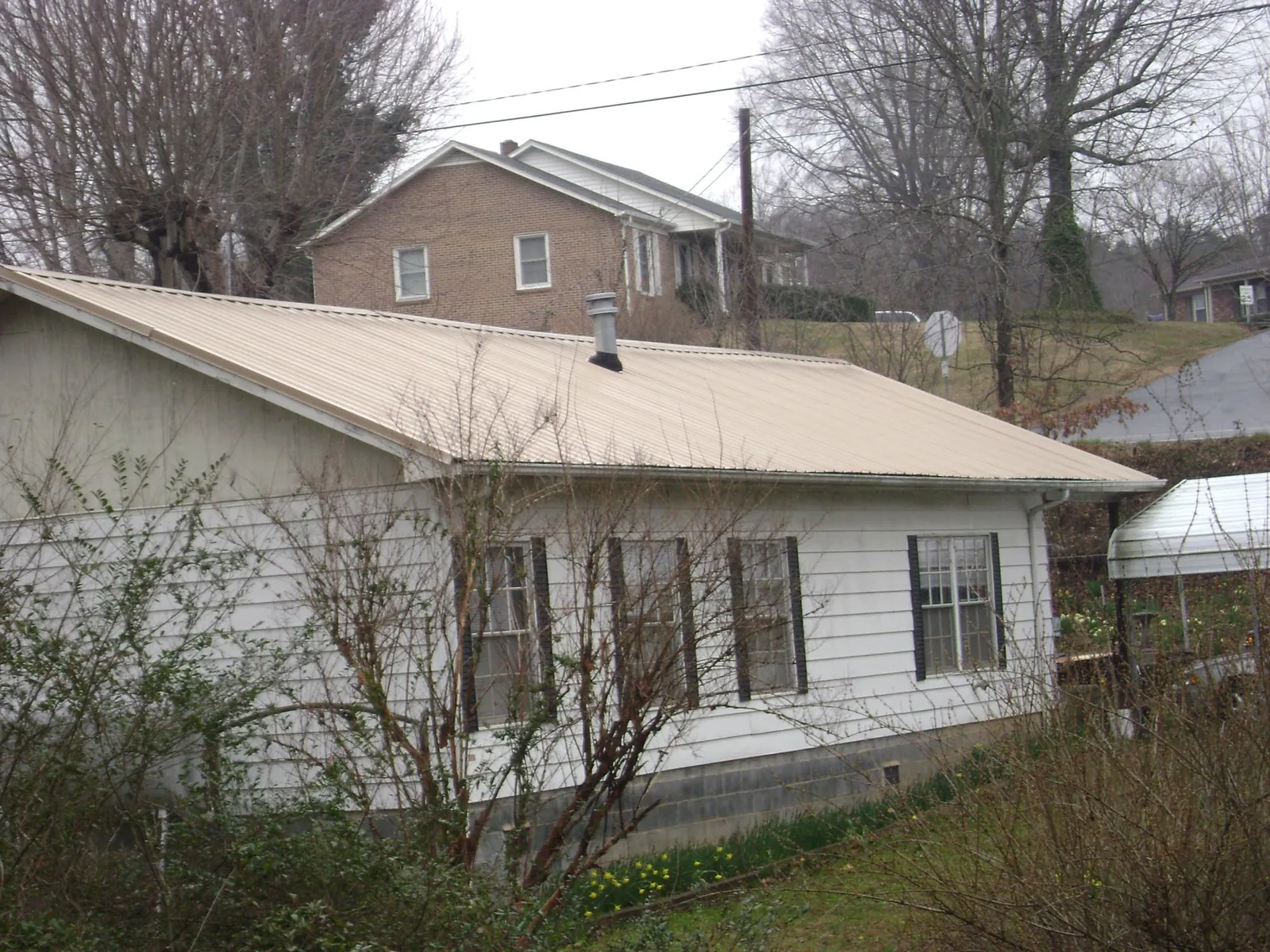 Tan metal roof on a white sided house set into a hillside — Commercial Roofing by Roofing Brothers in Mardela Springs